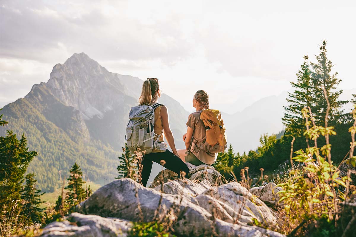 Experience the breathtaking Alps. Two hikers with rucksacks enjoy the view of the mountains during a break at the TRIFORÊT alpin.resort in Hinterstoder.