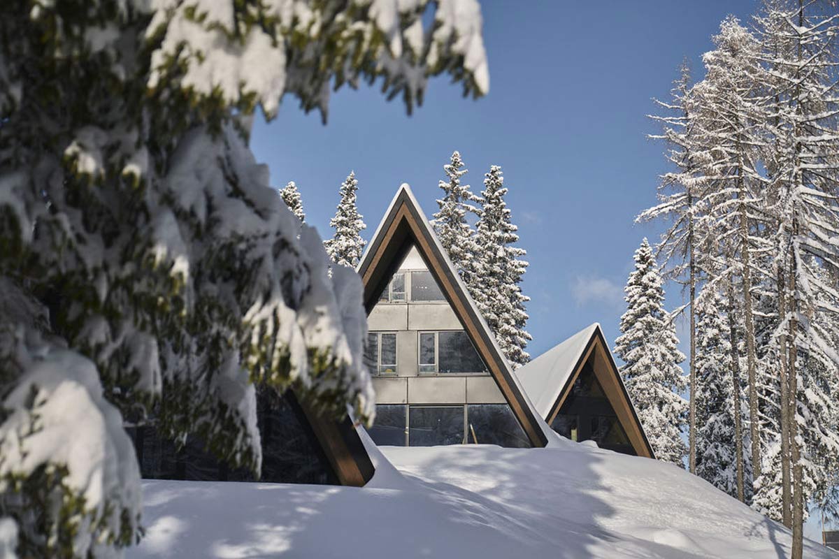 Pure mountain idyll - our chalets between snow-covered giant trees. Triangular chalet of the TRIFORÊT alpin.resort in Hinterstoder, surrounded by snow-covered trees in winter.