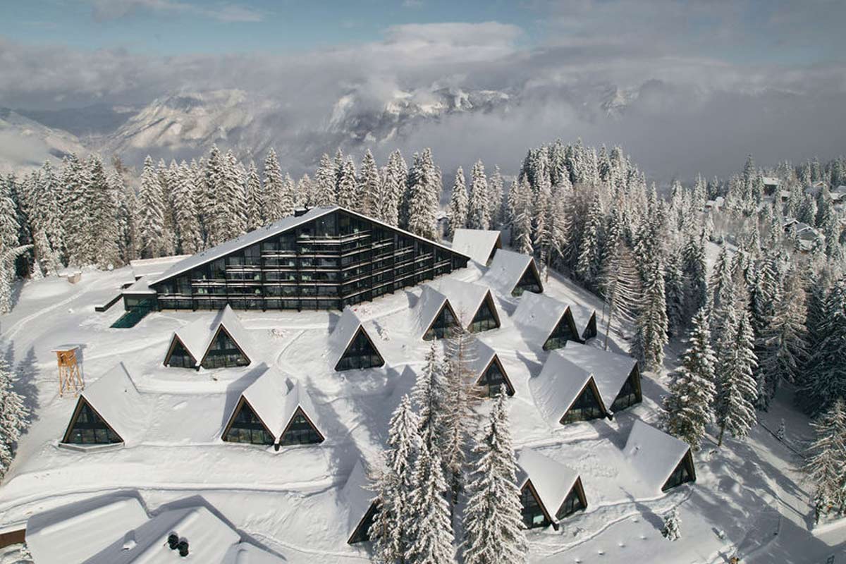 Winter wonder from above - our resort in the snowy Alpine panorama. Aerial view of the snow-covered TRIFORÊT alpin.resort with chalets and main building in the winter forest of Hinterstoder.