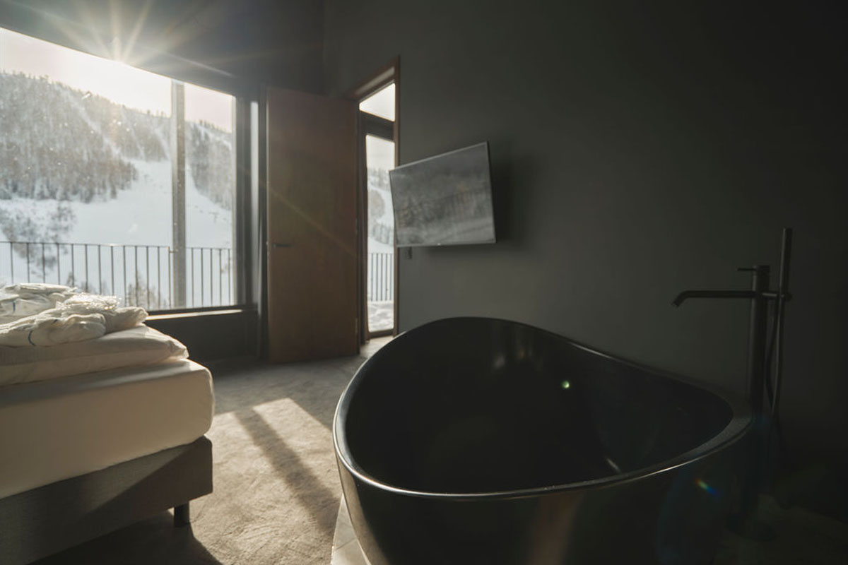 Pure relaxation with a view of the mountains. Free-standing black bathtub in the room with window view of snow-covered mountain slopes in the TRIFORÊT alpin.resort.