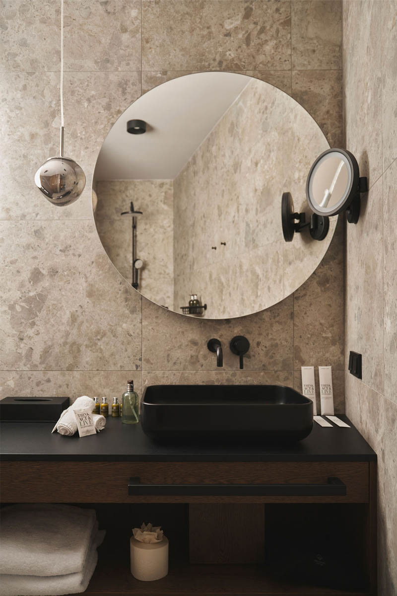 Mirror, stone & style - your elegant washplace in Hinterstoder. Modern washbasin with black mixer tap, large round mirror and stone wall in the TRIFORÊT alpin.resort.