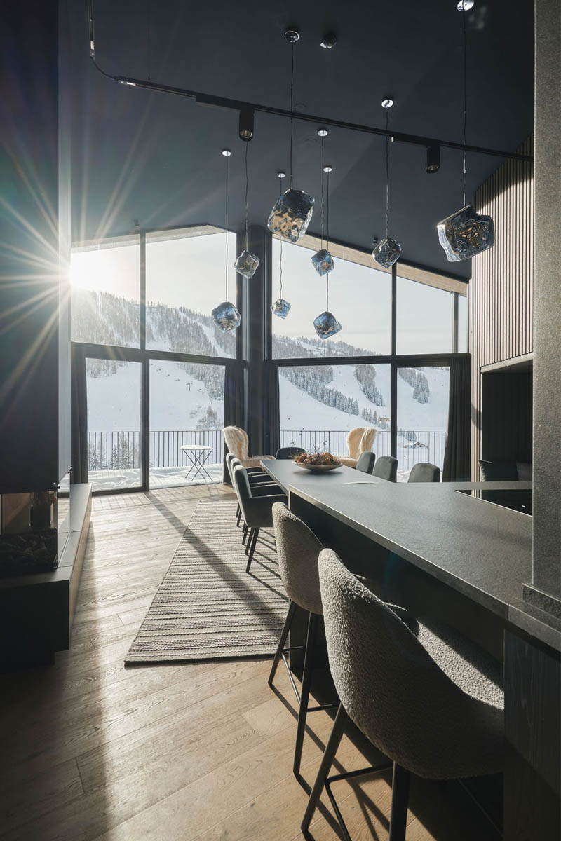 Wohnen mit Panoramablick im Urlaub in Hinterstoder. Innenaufnahme eines modernen Chalets im TRIFORÊT alpin.resort mit großem Fenster und Blick auf schneebedeckte Berge.