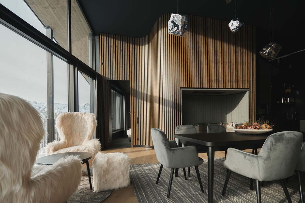 Entspannen Sie in unserem modernen Chalet mit Bergblick. Wohn- und Essbereich im Chalet im TRIFORÊT alpin.resort mit modernen Sesseln, Esstisch und Blick durch Panoramafenster.